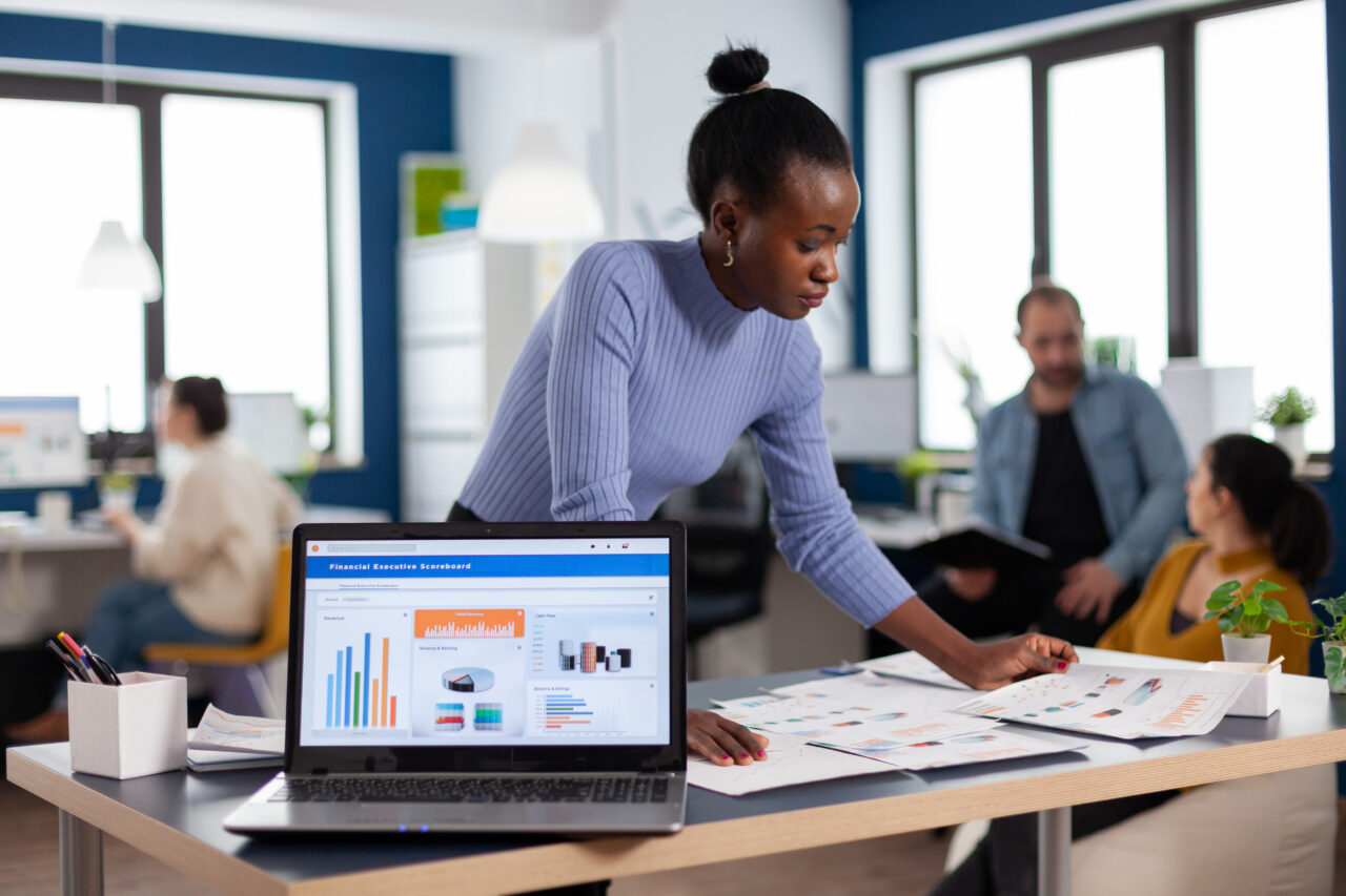 African entrepreneur of start up company reading charts on documents paperwork. Diverse team of business people analyzing company financial reports from computer. Successful corporate professional entrepreneur online internet statistics