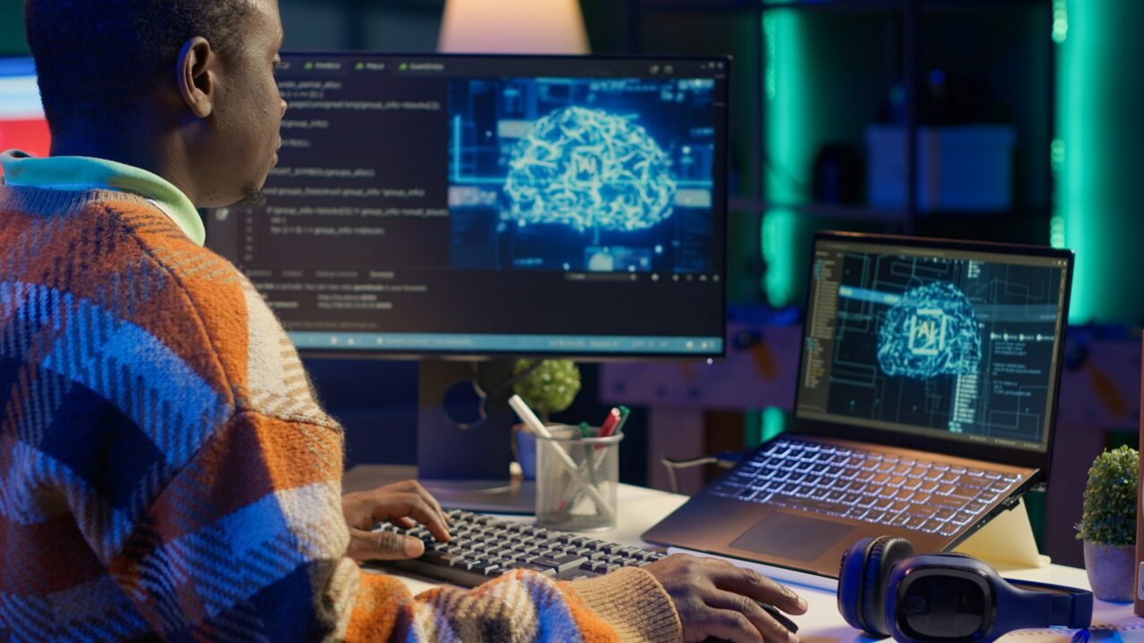 Black man programmer manages code and scripts in artificial intelligence and machine learning on dual monitors pc. Male freelancer uses personal computer to guarantee cyber security. Camera A.