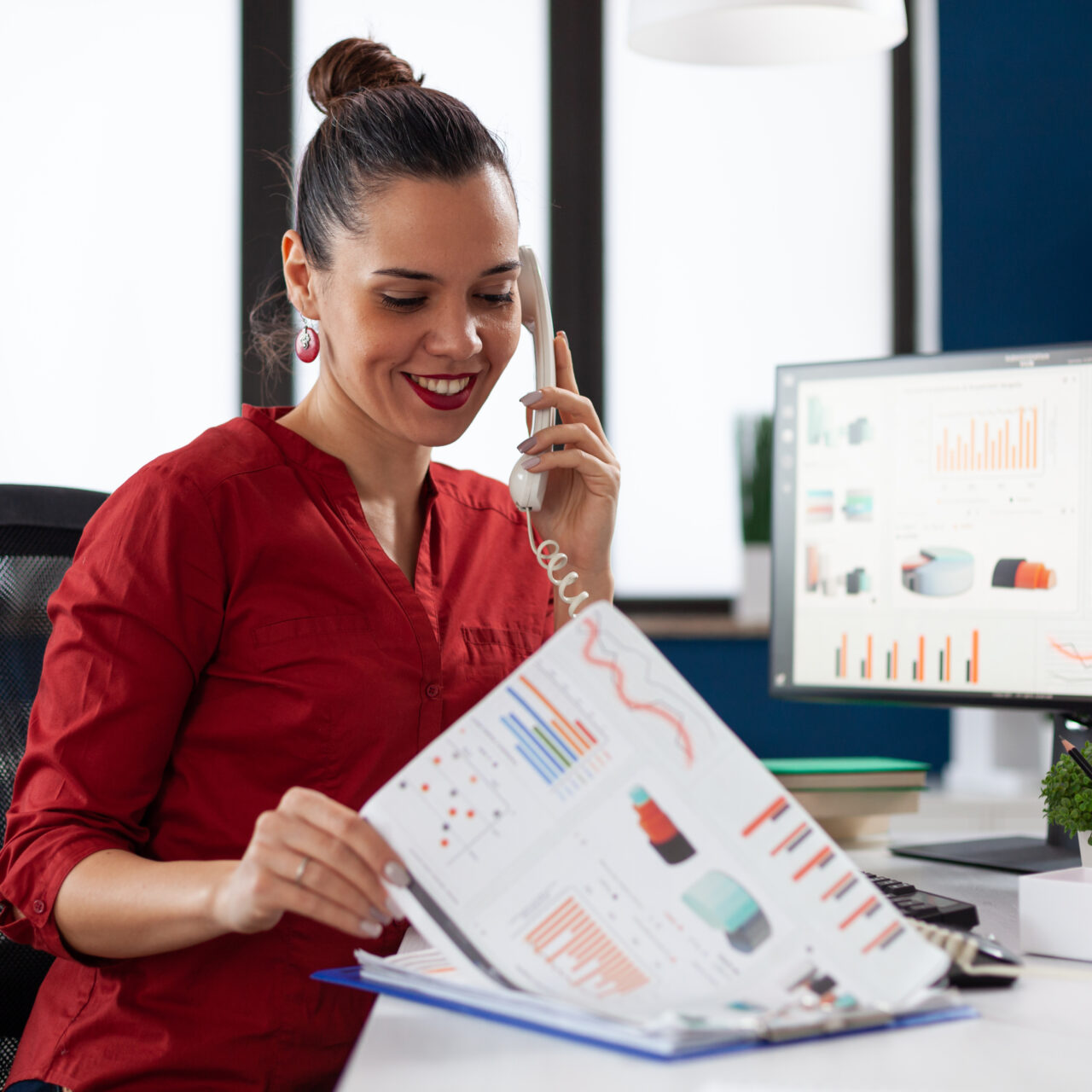Businesswoman in company office checking finaicial statistics on clipboard, discusing details with coworkers during phone call conversation. Happy entrepreneur communicating with client.